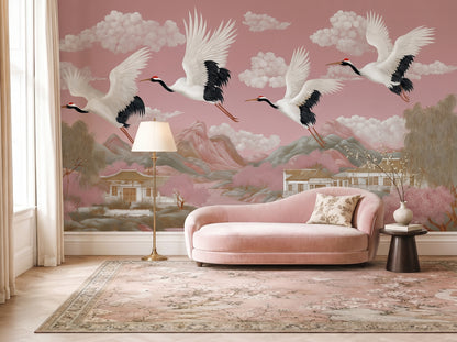 Blush pink chinoiserie crane wall mural in elegant living room with pink velvet sofa, featuring flying Japanese cranes, pagodas, mountains, cherry blossom trees, and panoramic Asian landscape wallpaper.